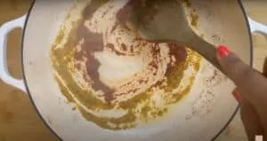 Stirring spices in a white Dutch oven with a wooden spoon on a stovetop, enhancing flavor.